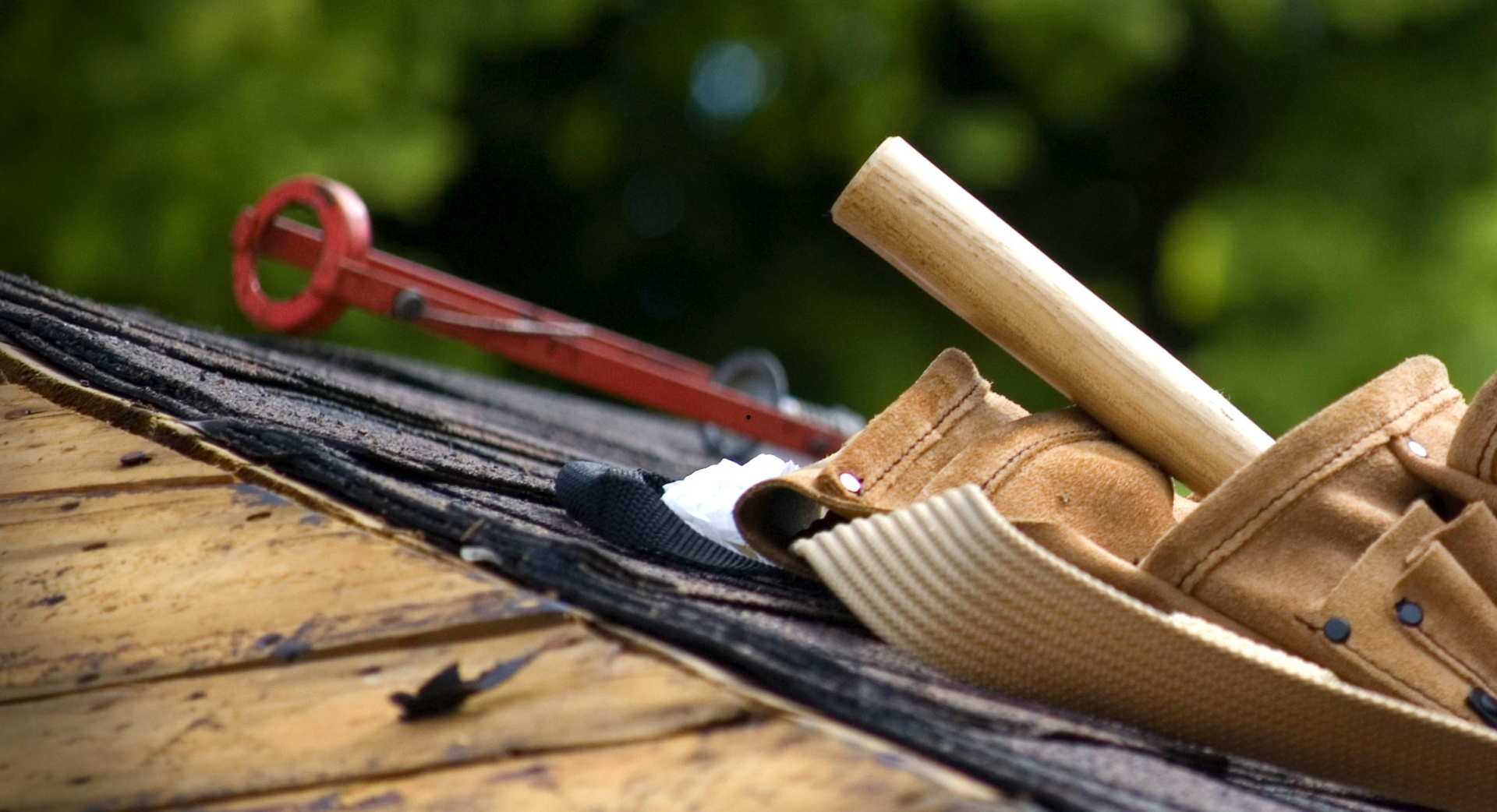 Ceinture à outils et outil rouge posés sur un toit patiné, avec un fond vert flou.
