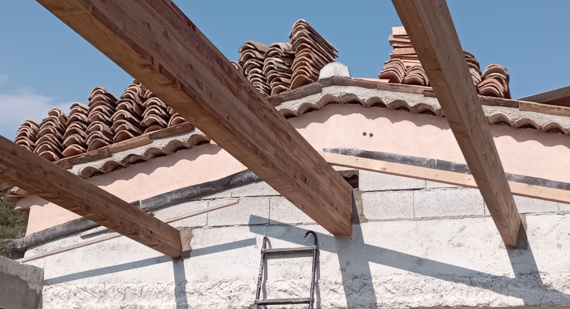 Poutres en bois s'étendant sur le toit d'un bâtiment, avec une pile de tuiles en argile en arrière-plan contre un ciel bleu.