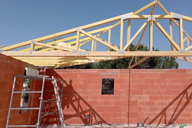 Ferme de toit en bois en cours de construction sur un bâtiment en briques rouges sous un ciel bleu clair.