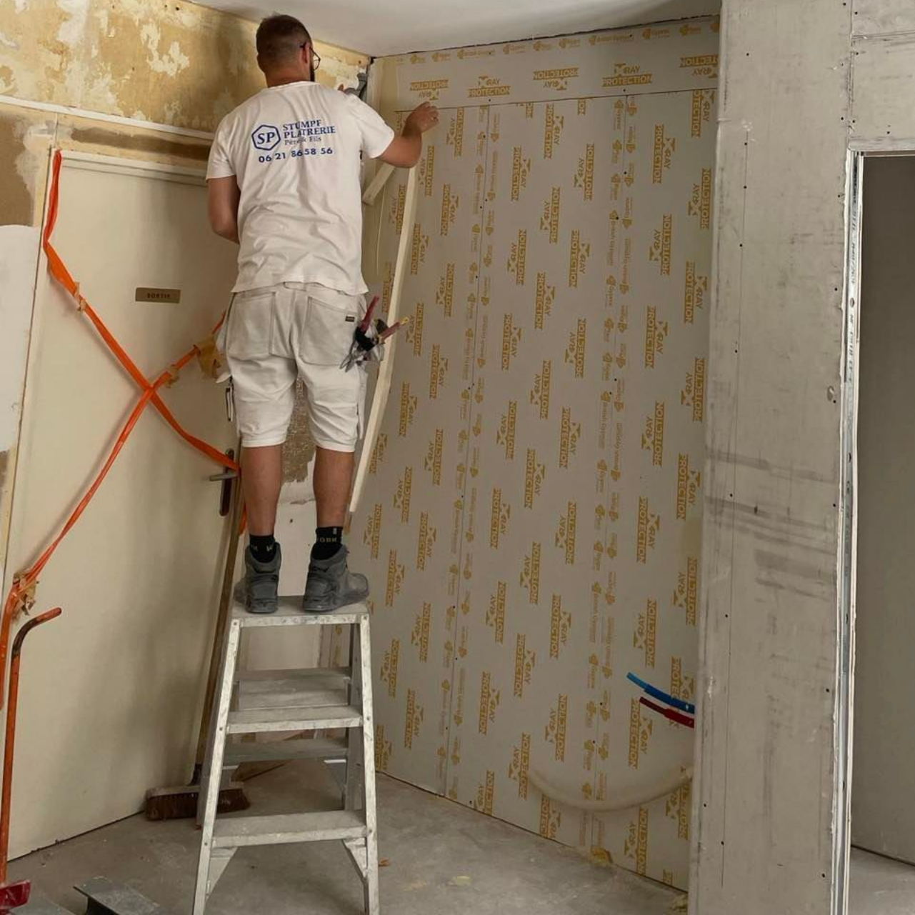 Ouvrier sur un escabeau, pose de membrane d'étanchéité à l'air sur un mur