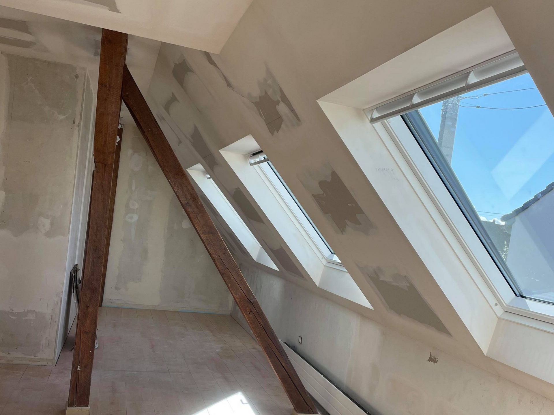 Travaux de plâtrerie pour aménager des combles, charpente en bois foncé et fenêtres de toit
