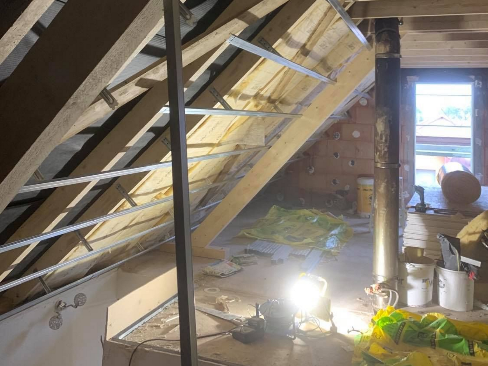 Projecteur de chantier éclairant un chantier d'isolation des combles, rails en métal sous charpente en bois