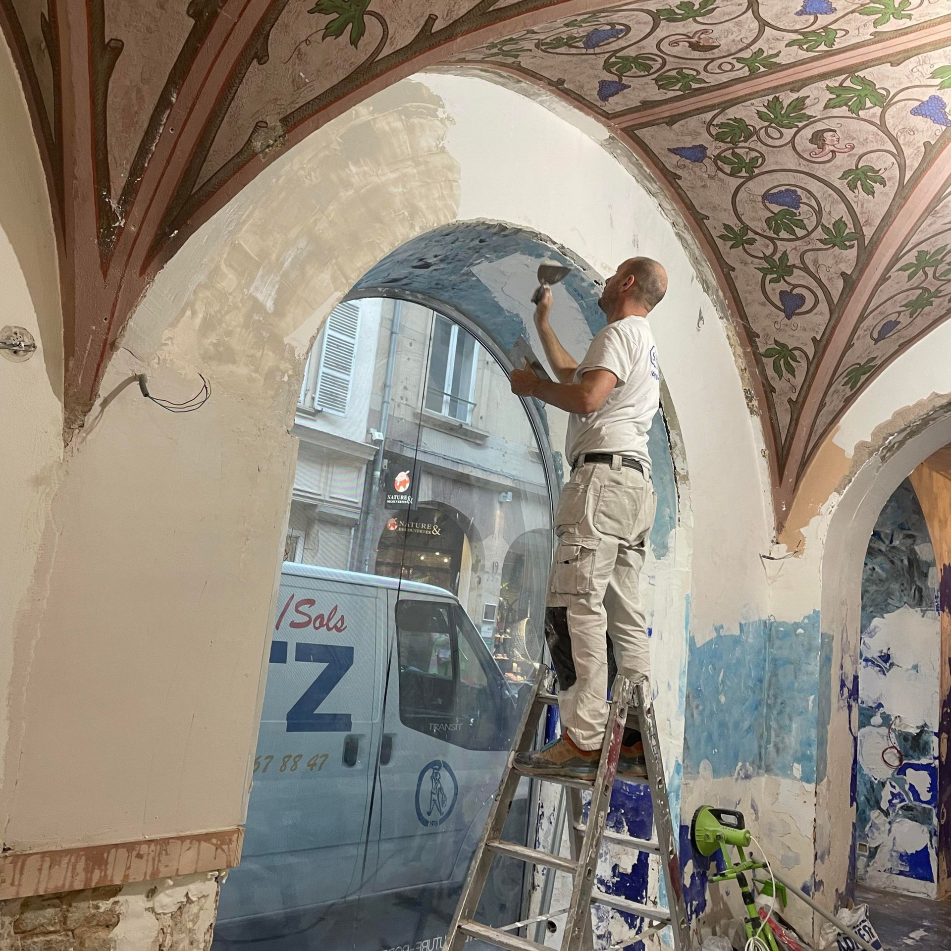 Rénovation de revêtement sur l'arche d'un bâtiment ancien, ouvrier sur un escabeau