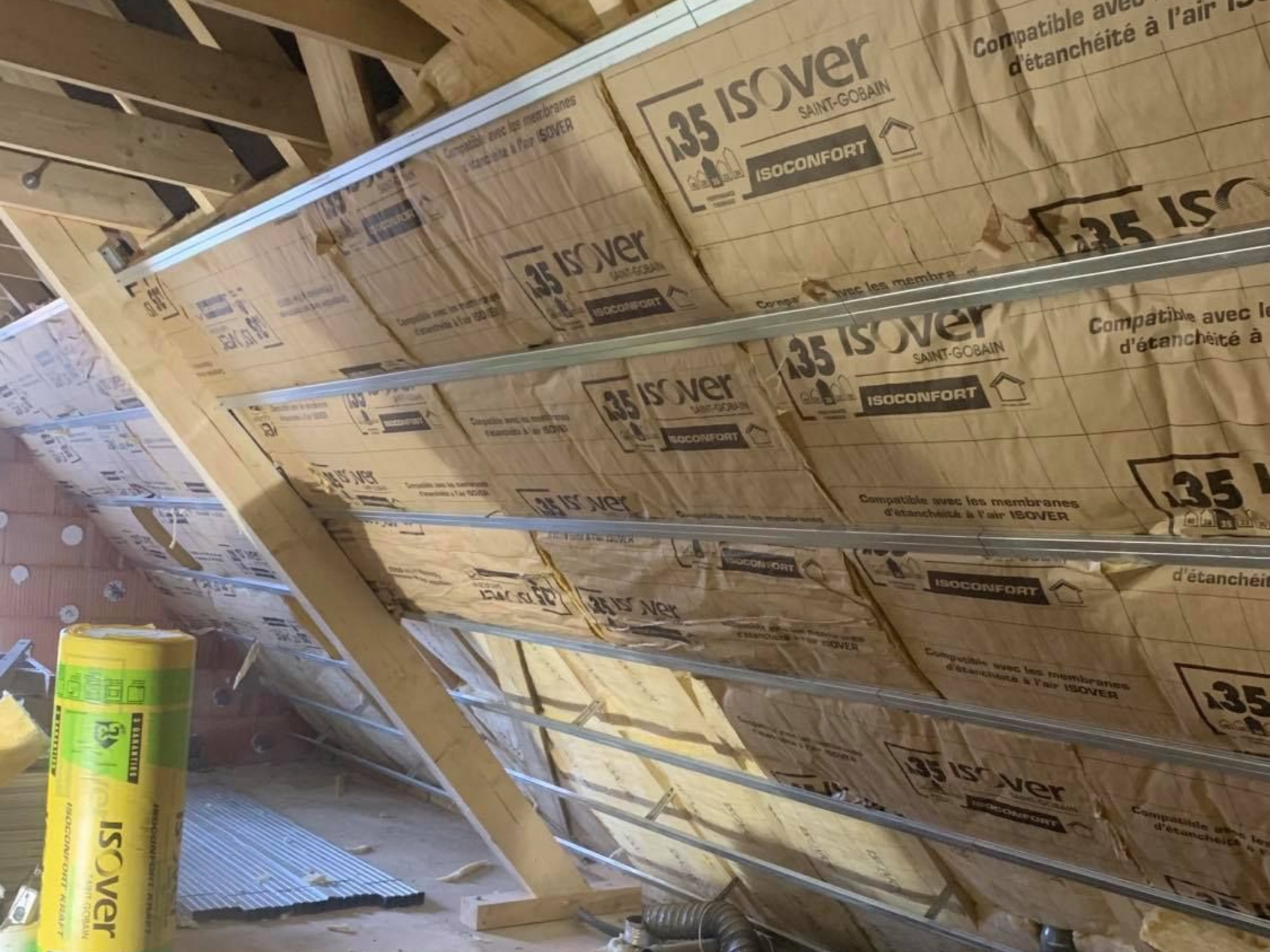 Isolation de combles aménagés, charpente en bois, rouleau d'isolant posé sur le sol