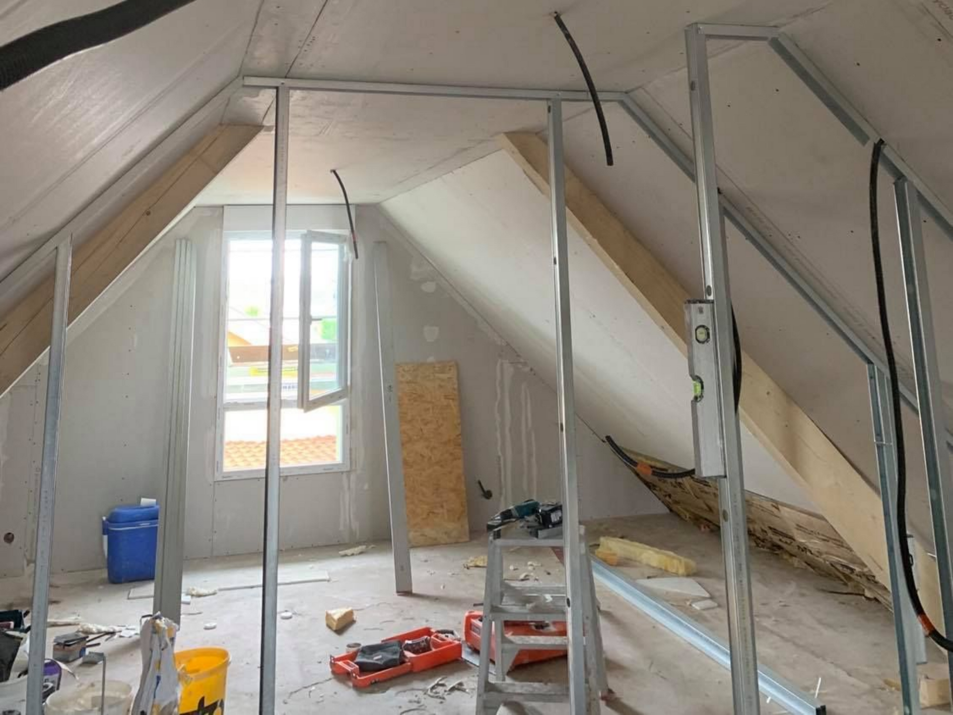 Travaux d'aménagement de combles, rails posés pour monter une cloison, outils sur le sol, fenêtre ouverte