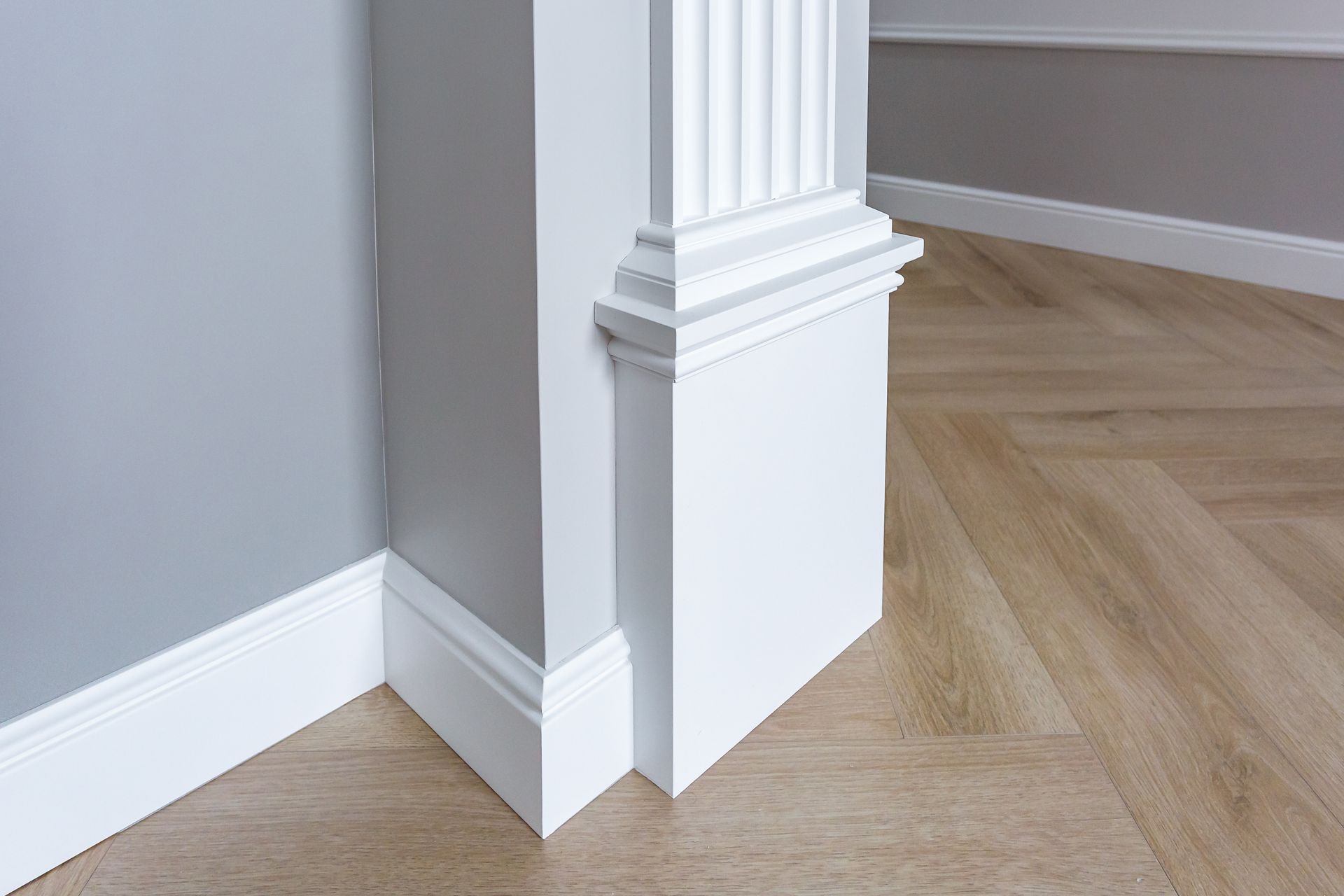 Moulure blanche sur un mur gris, parquet clair, plinthes blanches