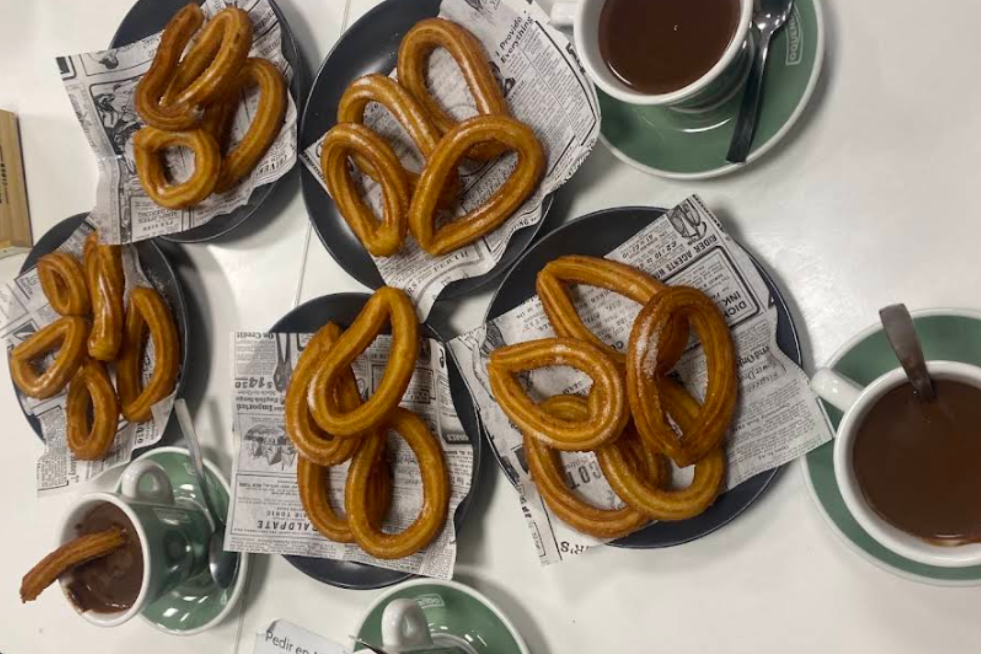 Una mesa cubierta con platos de churros y tazas de chocolate caliente.