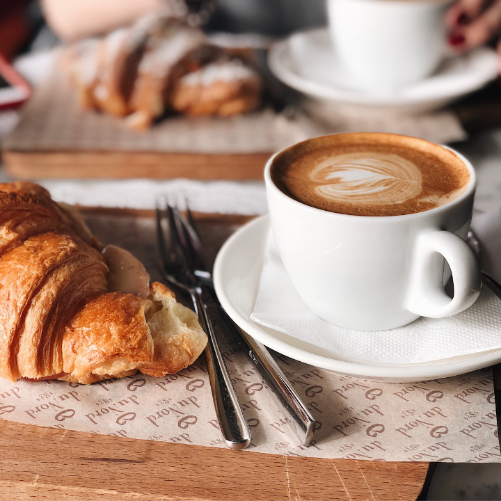 Un croissant junto a una taza de café en un platillo.