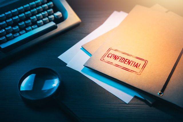 Machine à écrire, loupe et enveloppe estampillée Confidentiel sur un bureau, éclairé de façon théâtrale.