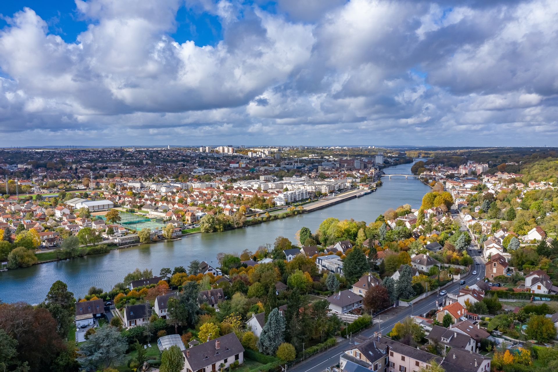Vue panoramique d'une rivière traversant un paysage urbain et rural sous un ciel nuageux.
