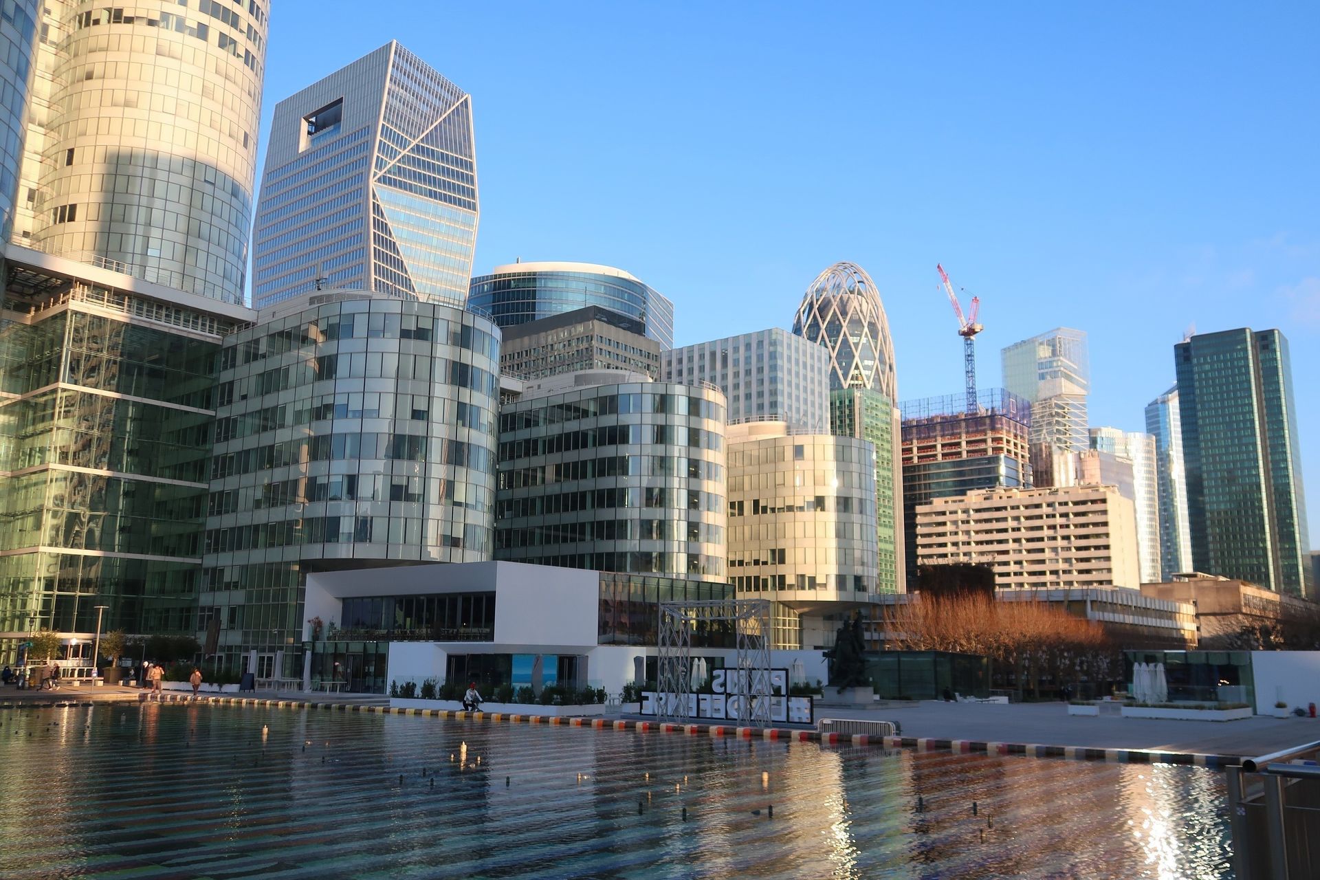 Des gratte-ciel modernes en verre se reflètent dans un bassin sous un ciel bleu azur.
