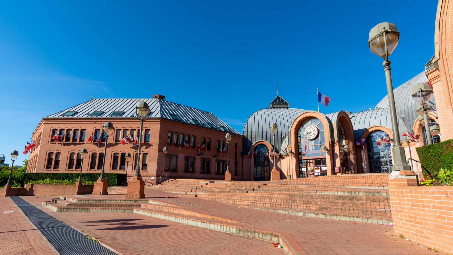 Des bâtiments en briques à l'architecture variée, des drapeaux et un ciel bleu.