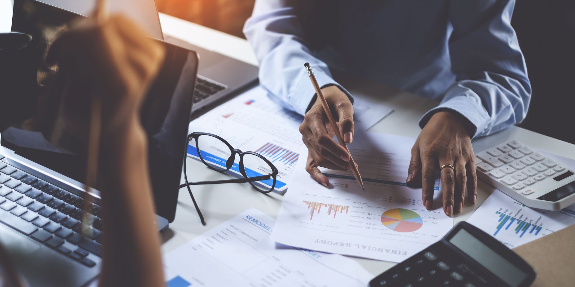 Deux personnes examinent des documents financiers, à l'aide d'une calculatrice et d'un ordinateur portable, à un bureau.