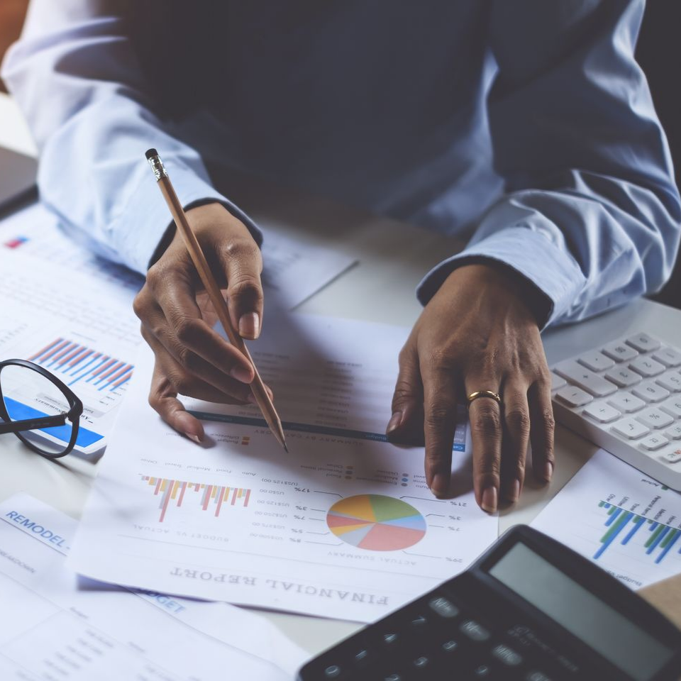 Une personne examine des rapports financiers, pointant du doigt un graphique circulaire avec un crayon, une calculatrice et un clavier étant visibles.