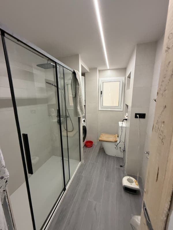 Baño moderno con ducha de cristal, inodoro y suelo gris en un pasillo estrecho con vistas