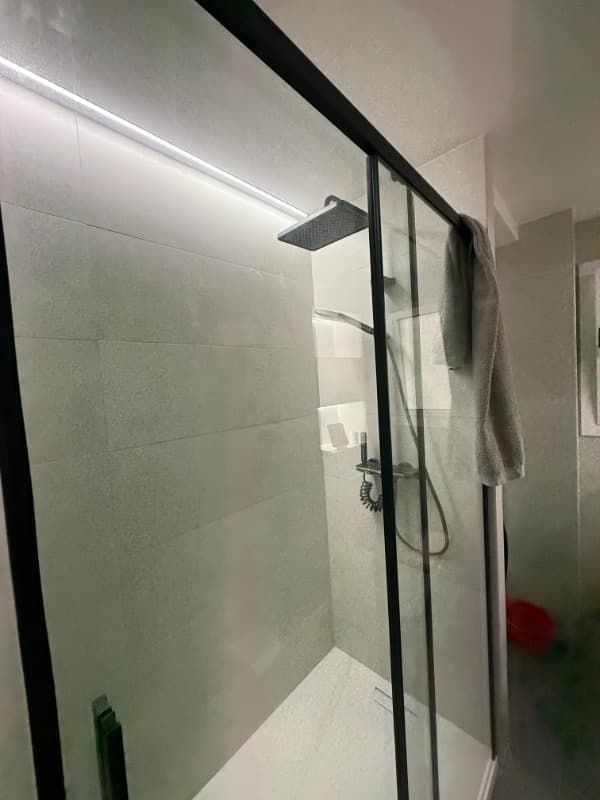 Baño moderno con ducha, mampara de cristal, cabezal de ducha mural y toallero en la puerta.