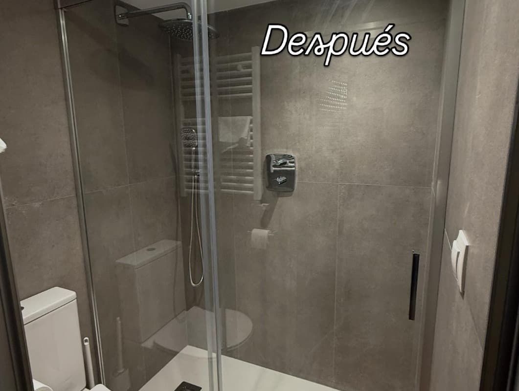 Vista de un baño moderno con ducha de vidrio y la palabra “Después” en la pared.