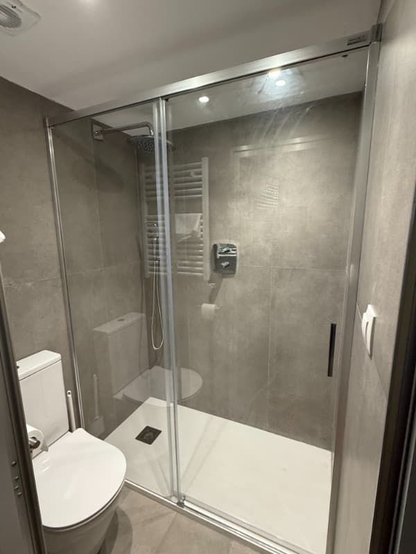 Baño moderno con cabina de ducha de cristal, azulejos grises y un inodoro a la izquierda.