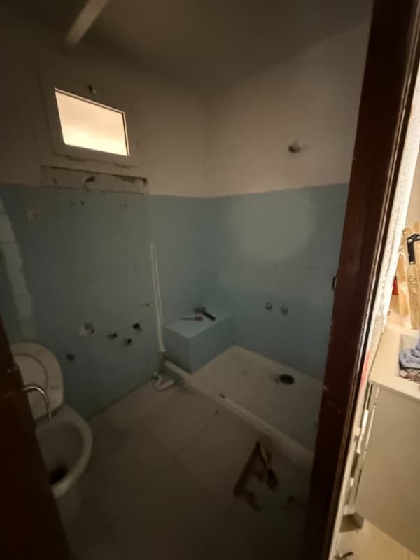 Baño pequeño en obras con paredes inferiores azules, inodoro, bañera y ventana.