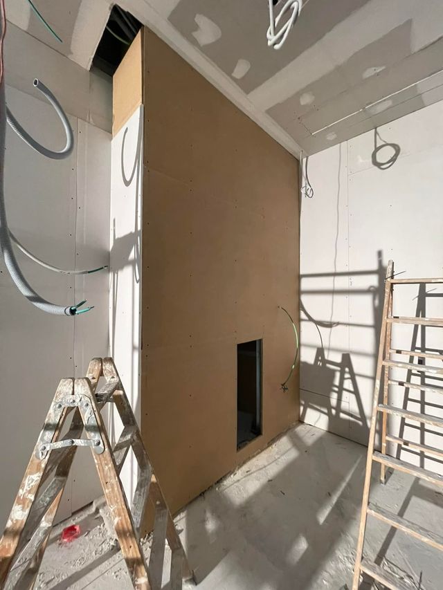 Obra en construcción con una gran pared divisoria de pladur marrón, escaleras y andamios en una habitación luminosa sin terminar.
