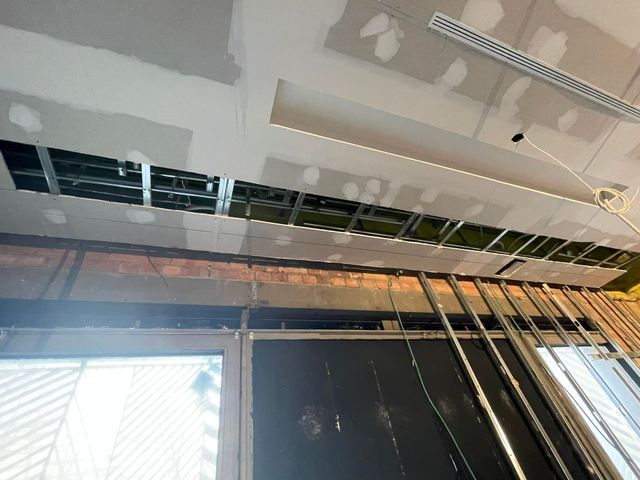 Techo con cableado a la vista y una lámpara colgante sobre una puerta en una habitación en renovación.