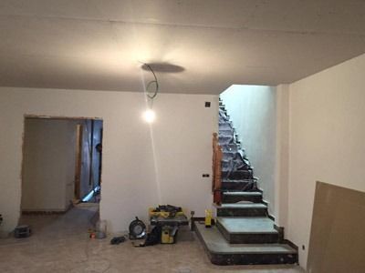 Habitación sin terminar con suelo desnudo, bombilla a la vista y escaleras que suben a la derecha.
