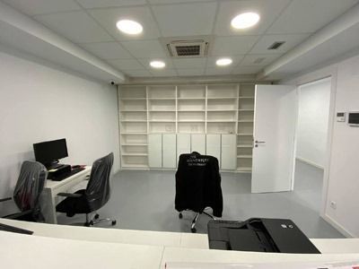 Oficina moderna vacía con escritorios, sillas, estanterías y luces empotradas brillantes en el techo.