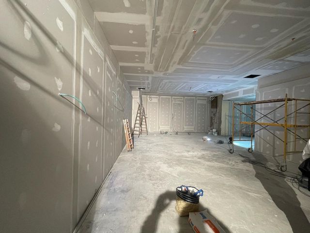 Habitación sin terminar, en construcción, con andamios, escalera y herramientas sobre un suelo cubierto de polvo.