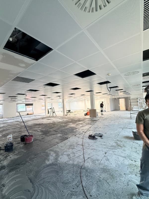 Interior de oficina parcialmente renovado con techo de baldosas a la vista, suelo desnudo y materiales de construcción.