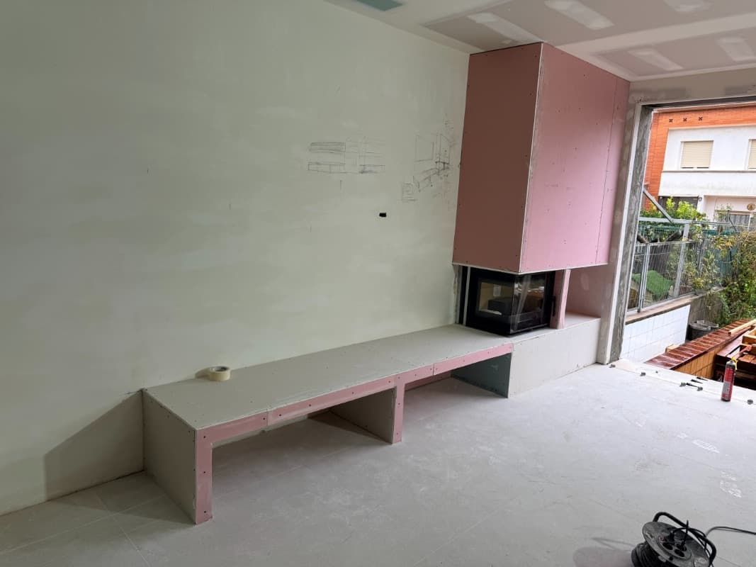 Habitación vacía con un banco rosa empotrado y un nicho en la pared, que da a un balcón con plantas.