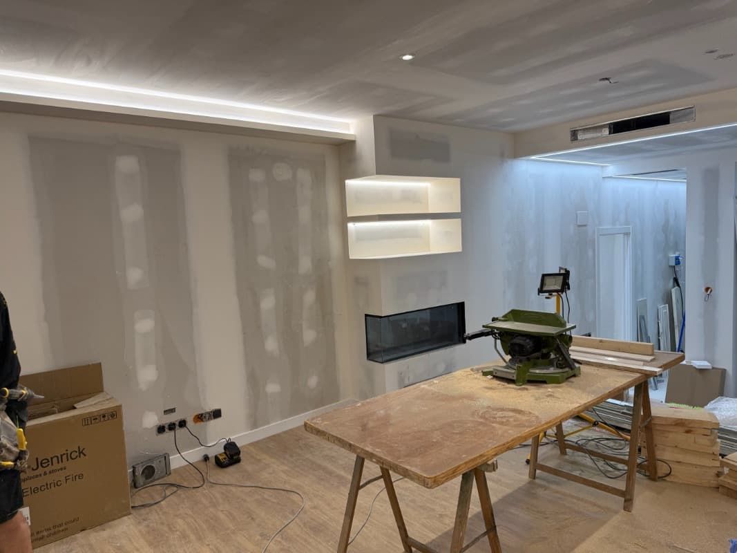 Sala de estar moderna en renovación con paredes revestidas de plástico, una mesa de trabajo y materiales de construcción.