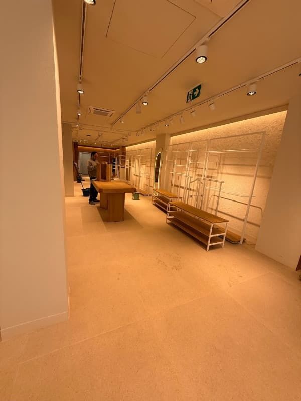 Interior de tienda vacío con iluminación cálida, con estanterías y mesas de exposición en construcción.