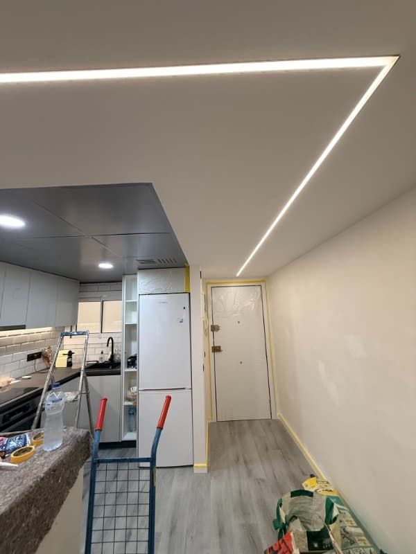 Cocina moderna en proceso de renovación con herramientas, escalera, gabinetes blancos e iluminación de tiras en el techo.