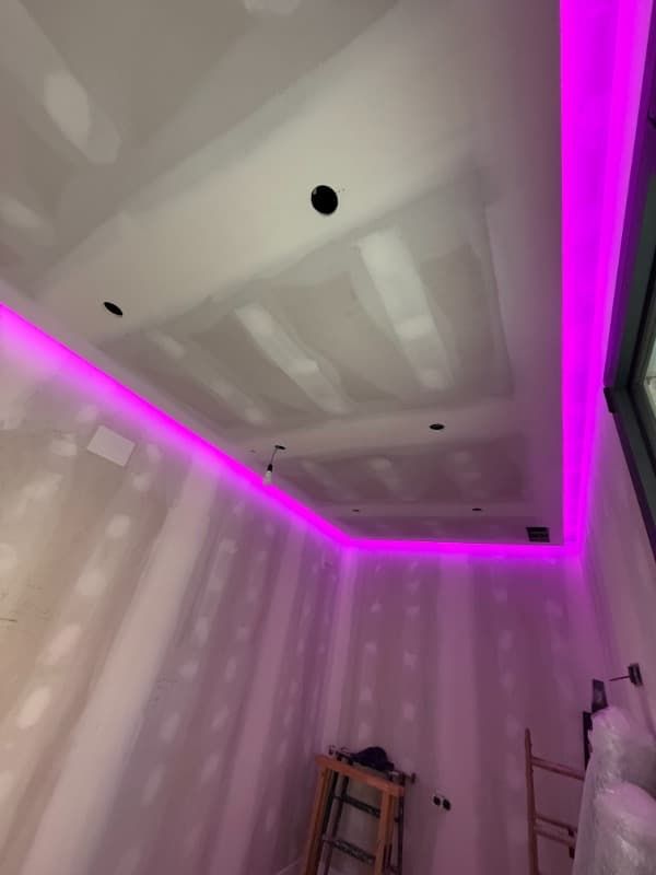 Techo de la habitación parcialmente terminado con iluminación LED de tira morada y parches de paneles de yeso.