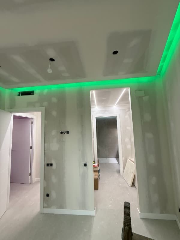 Habitación sin terminar con paredes blancas, luces LED verdes en el techo y puertas abiertas que dan a las habitaciones contiguas.