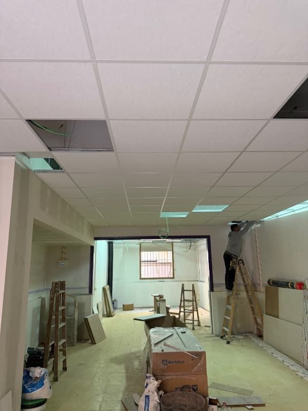 Espacio de trabajo para reformas con falso techo, escaleras, herramientas y materiales de construcción en una habitación larga.