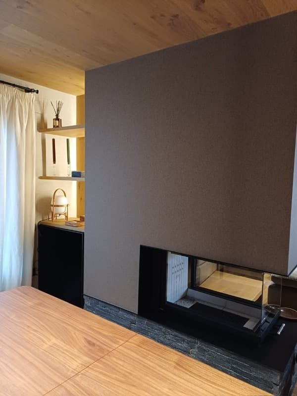 Sala de estar moderna con chimenea empotrada oscura, techo de madera y estanterías junto a una ventana con cortinas.