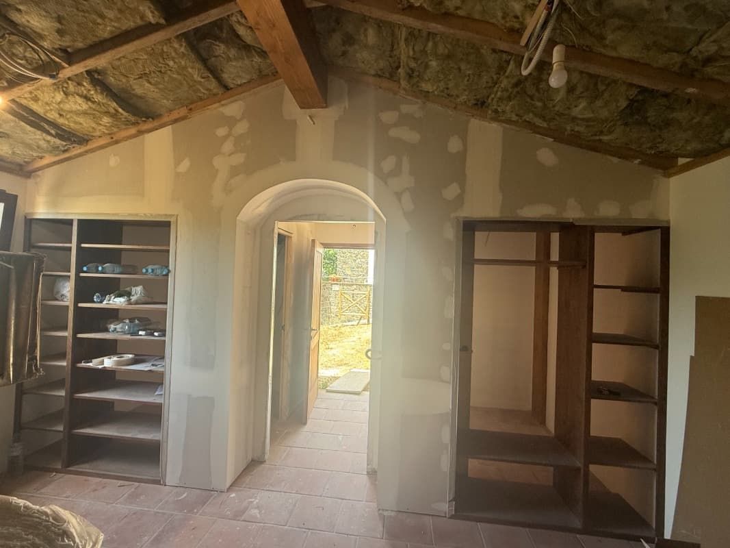 Habitación con poca luz, vigas de madera a la vista, puerta arqueada y estanterías empotradas en las paredes.