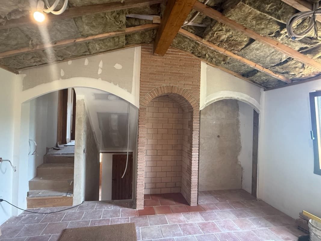Habitación reformada con vigas a la vista, arco de ladrillo, escaleras a la izquierda y paredes de yeso sin terminar.