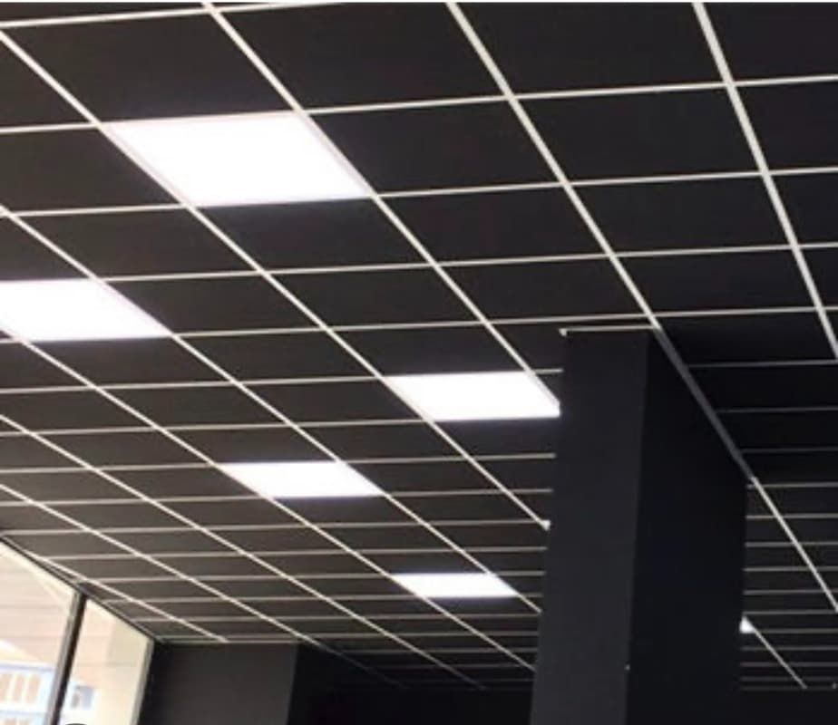 Techo de rejilla negra con luces rectangulares brillantes y una columna de soporte oscura.