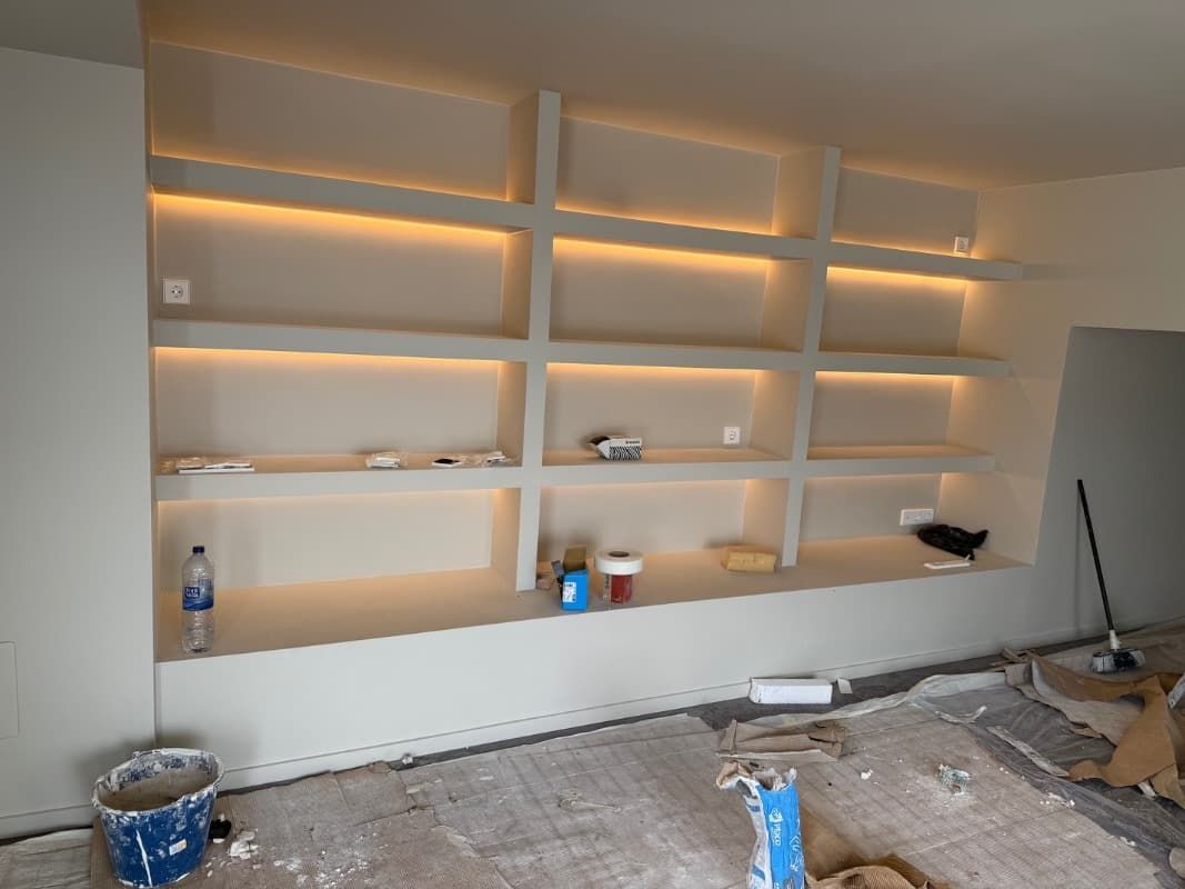 Estanterías empotradas parcialmente terminadas con iluminación cálida en una habitación en proceso de renovación.