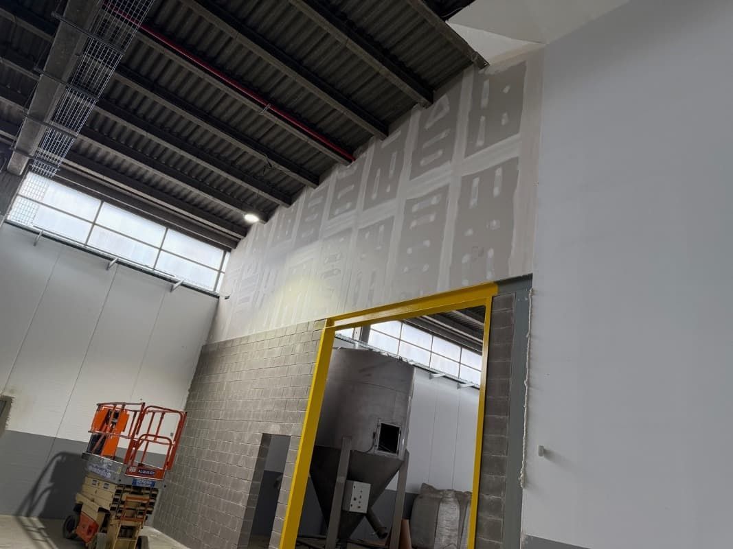 Interior de un almacén en construcción, donde se aprecian las paredes de pladur, las vigas del techo a la vista y una puerta con marco amarillo.