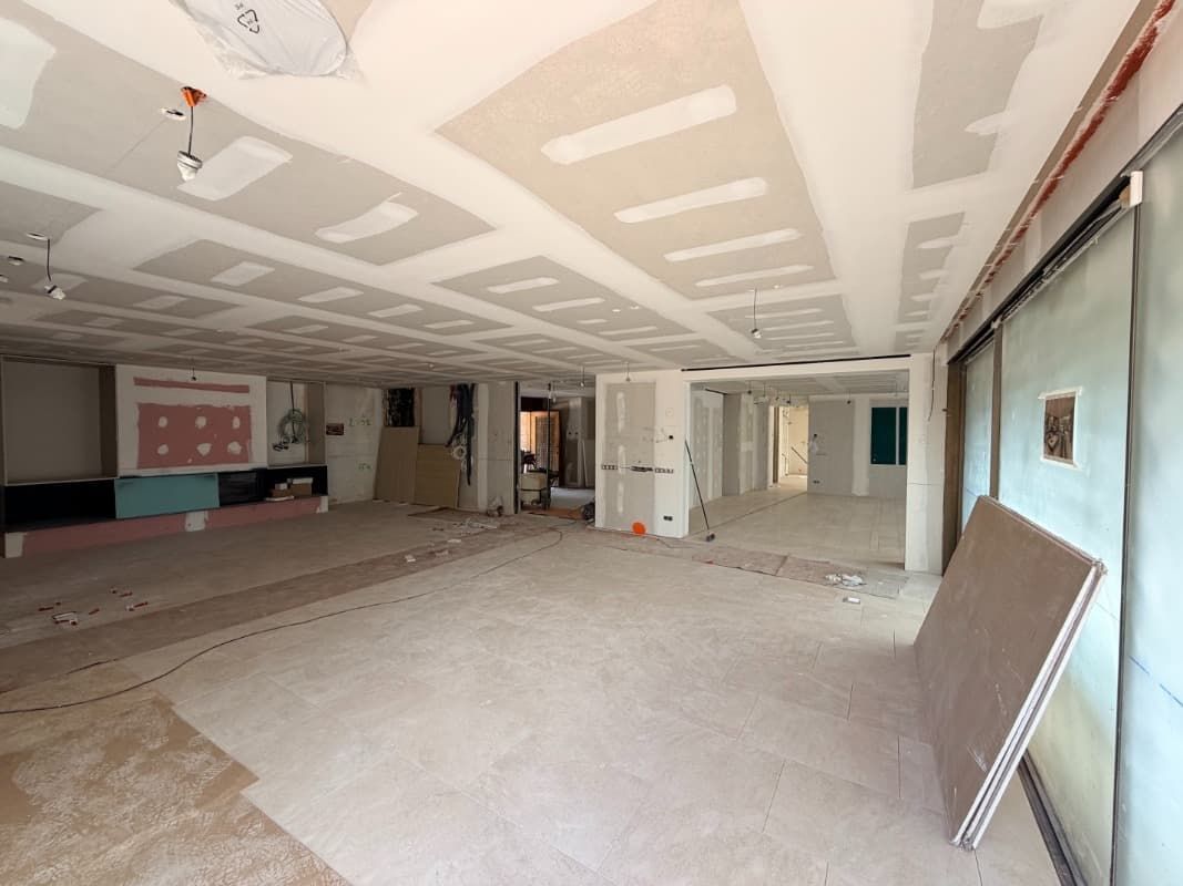 Habitación vacía sin terminar con paneles de yeso, paneles de techo, materiales de construcción y grandes ventanas a la derecha.