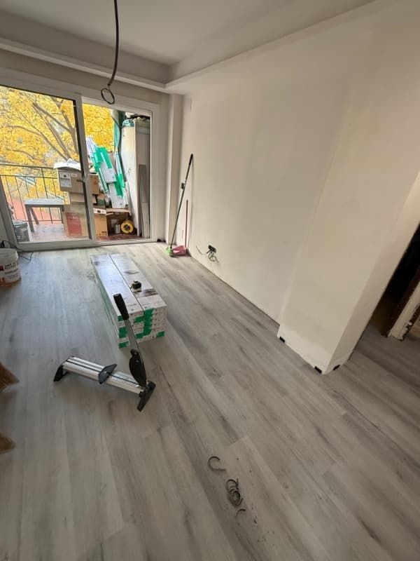 Habitación vacía con suelo de madera gris, materiales de pintura y una puerta con una ventana luminosa.