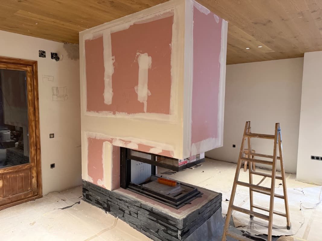 Habitación parcialmente terminada con chimenea, parches de yeso rosa y una escalera de madera a la derecha.