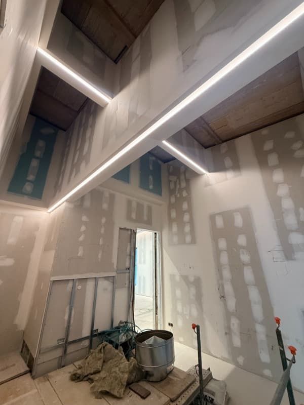 Interior sin terminar, con parches en las paredes de yeso, vigas de techo a la vista y materiales de construcción en el suelo.