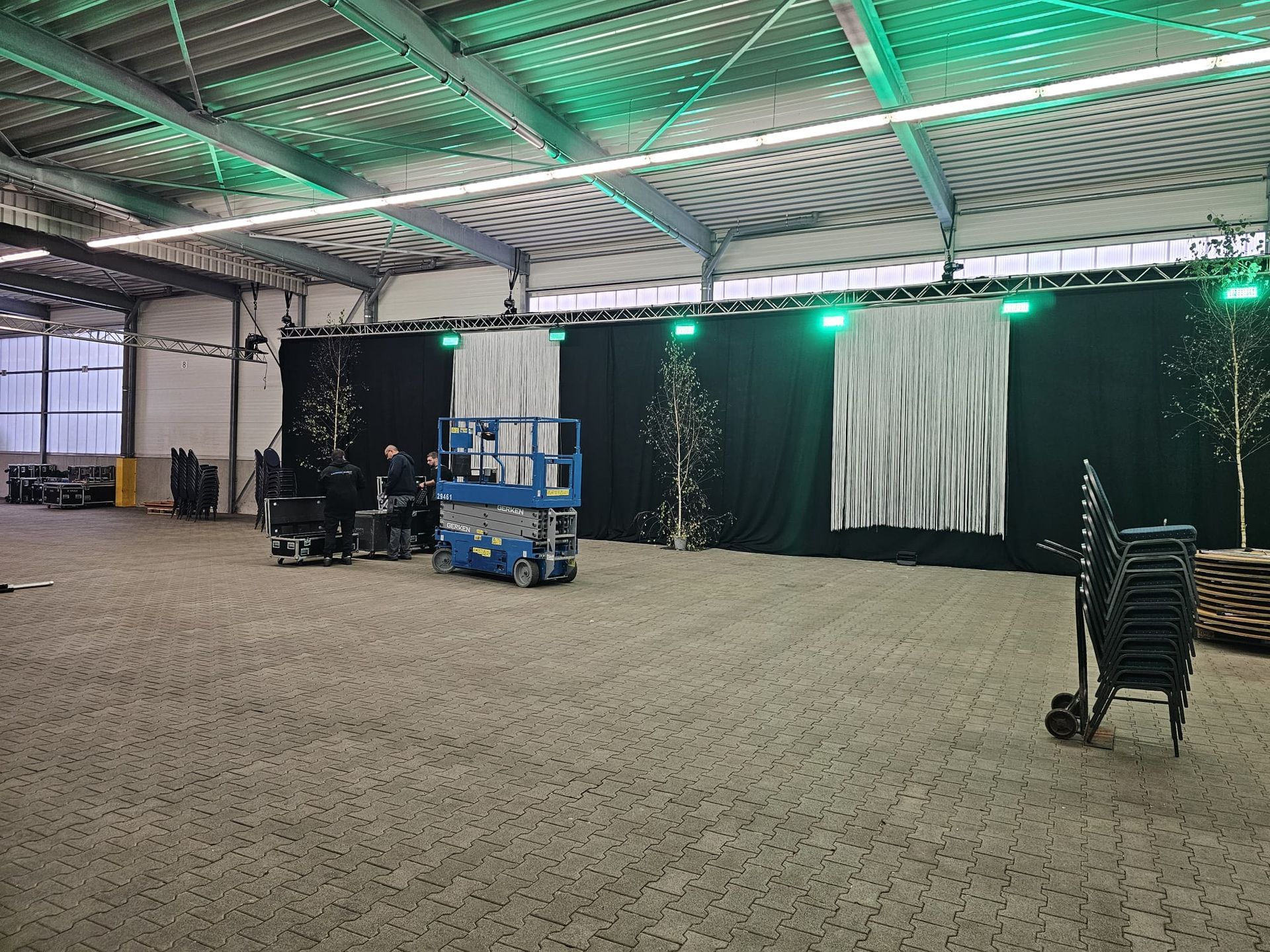 Eine leere Lagerhalle mit Bühnenaufbau, einschließlich schwarzer Vorhänge, Bäume und Beleuchtung.