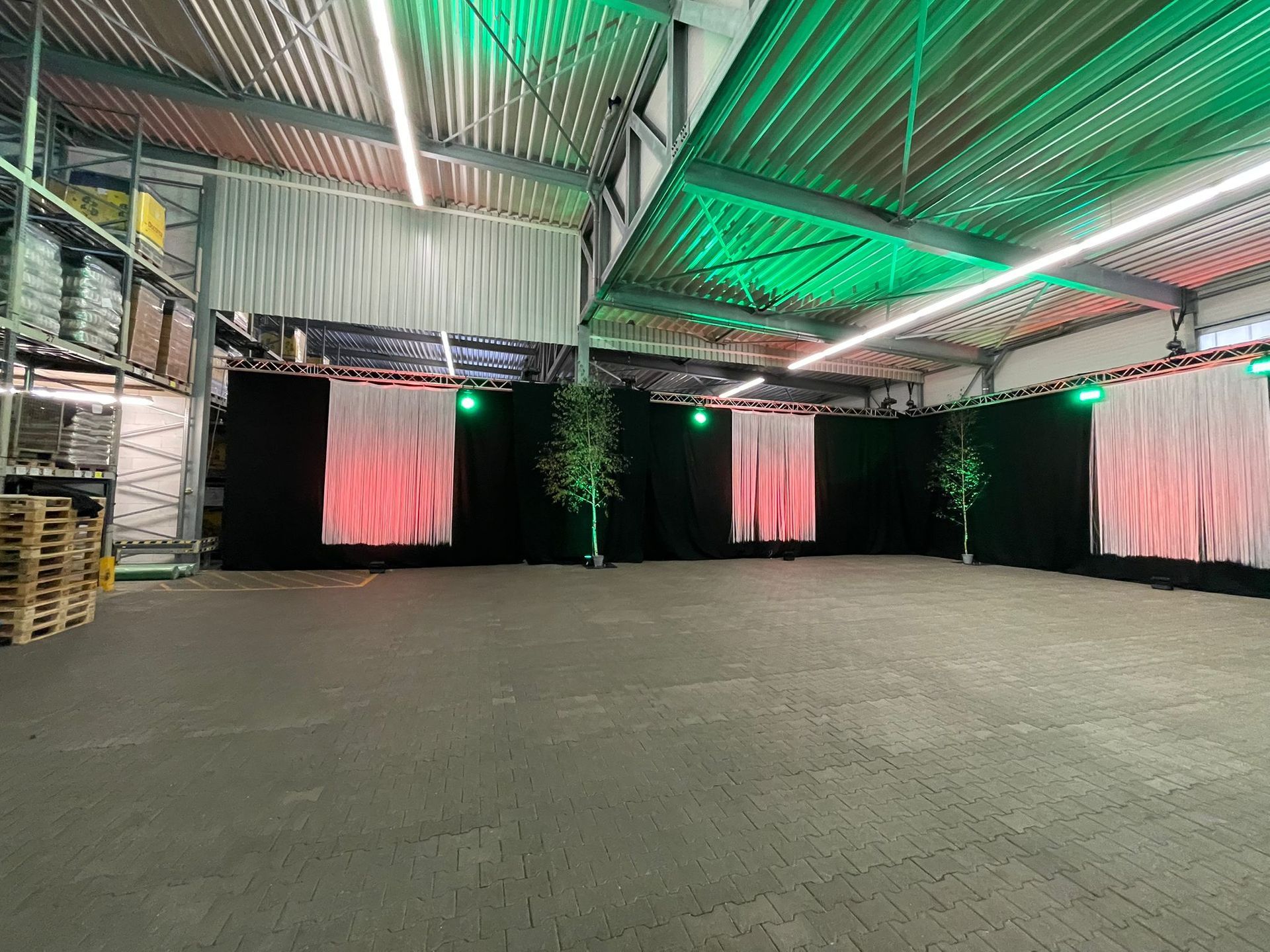 Leeres Lagerhalleninneres mit schwarzem Hintergrund, weißen Vorhängen, grüner und roter Beleuchtung.