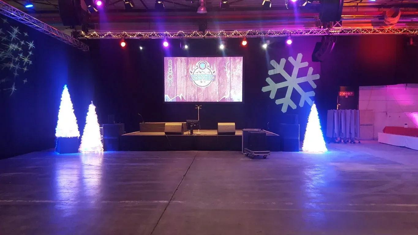 Eine leere Locationhalle mit Weihnachtsbäumen und Strahlern mit Schneeflocken