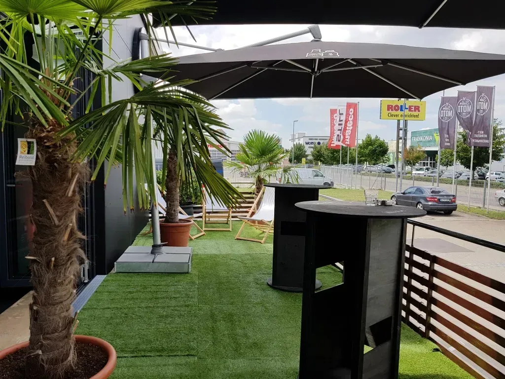 Eine Terrasse mit Tischen und Palmen und einem großen Regenschirm als Eventdekoration